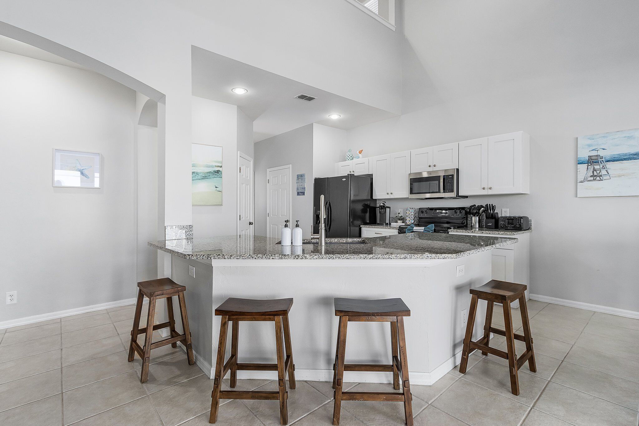 Una cocina moderna con armarios blancos, una isla grande con taburetes y vistas al área de estar.
