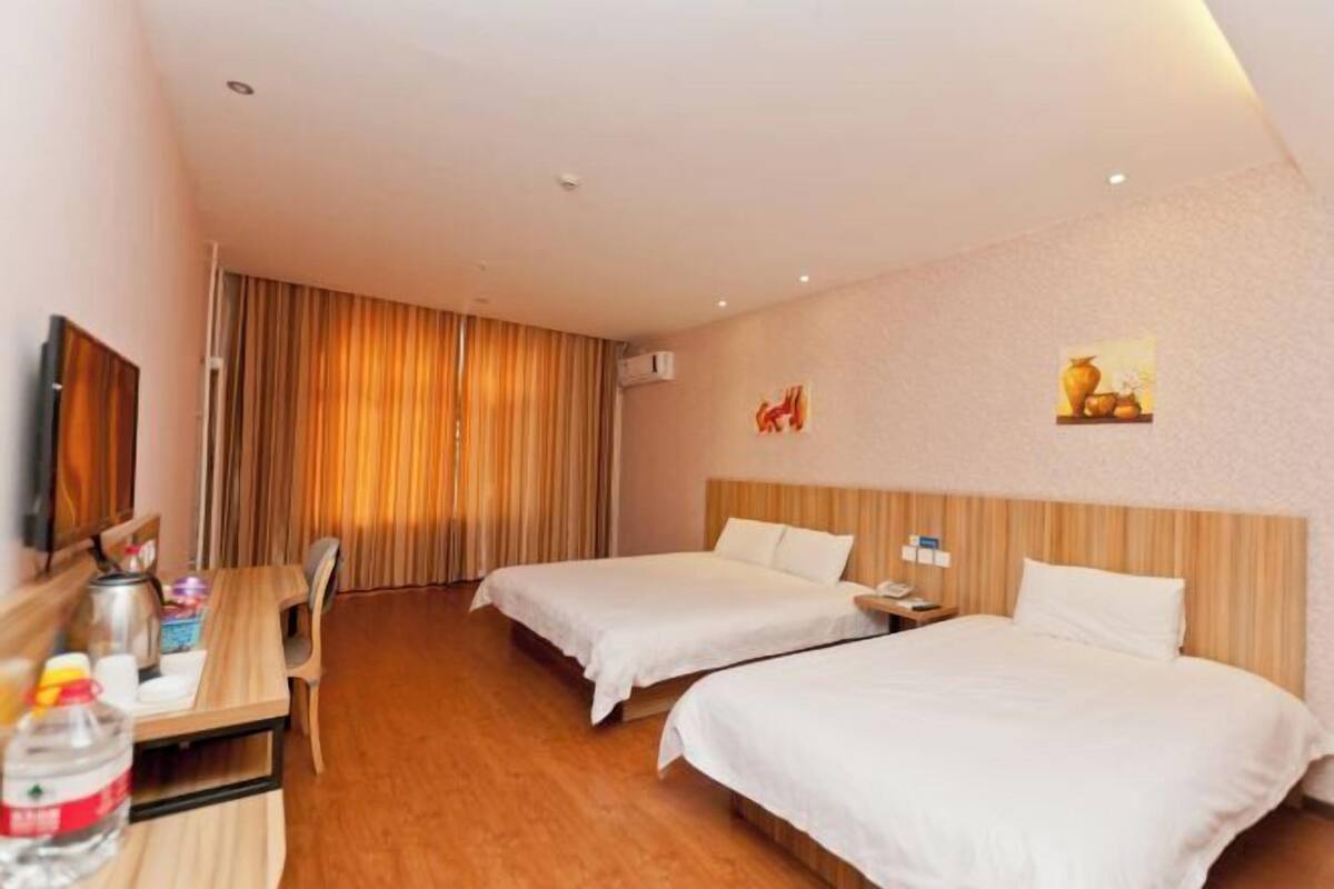 Une chambre d’hôtel avec deux lits, un bureau en bois, une chaise, une télévision et un tableau au mur.