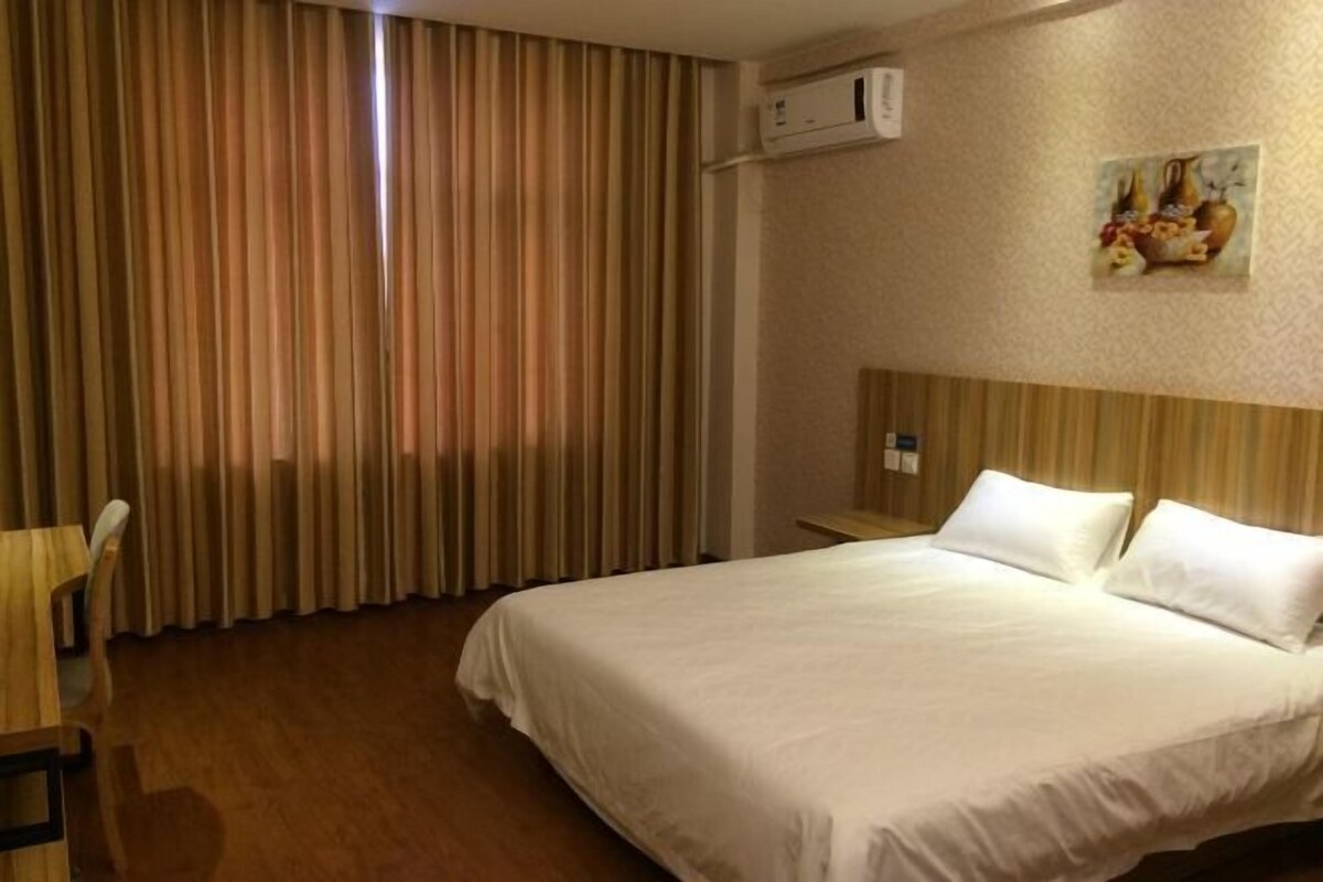 A hotel room with a large bed, a wooden nightstand, a chair, a painting on the wall, and a window with curtains.