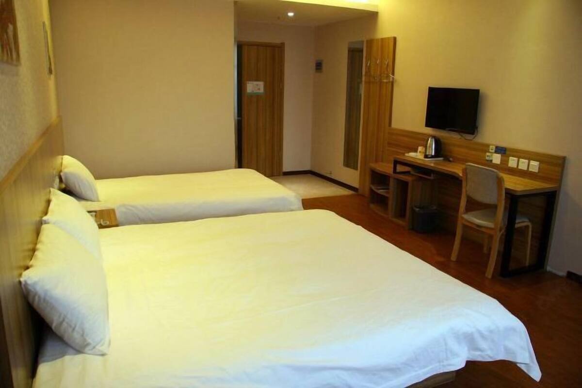 Une chambre d’hôtel avec deux lits simples, un bureau avec une chaise, une télévision et une armoire en bois.