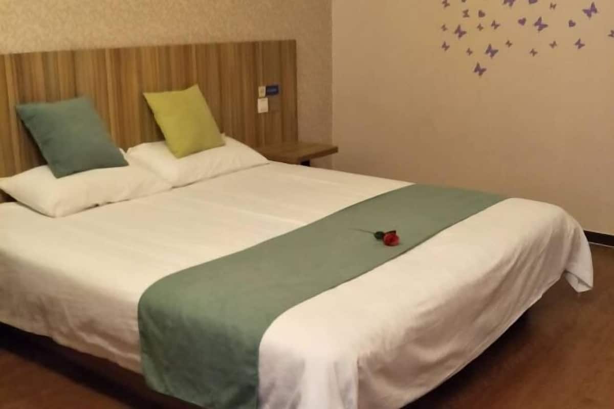 Un lit bien fait, recouvert d’une couverture verte et blanche, avec un seul oreiller et une petite rose rouge posée sur le lit.