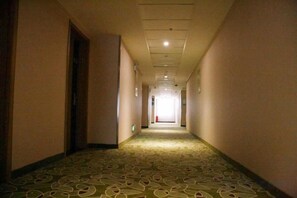 Pasillo de hotel con piso alfombrado, puertas a ambos lados y una fuente de luz al final.