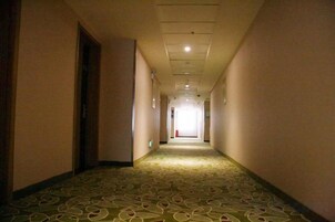 Pasillo de hotel con piso alfombrado, puertas a ambos lados y una fuente de luz al final.