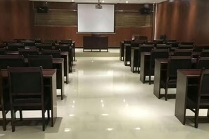 Un salón de conferencias con filas de sillas mirando hacia una pantalla de proyección.