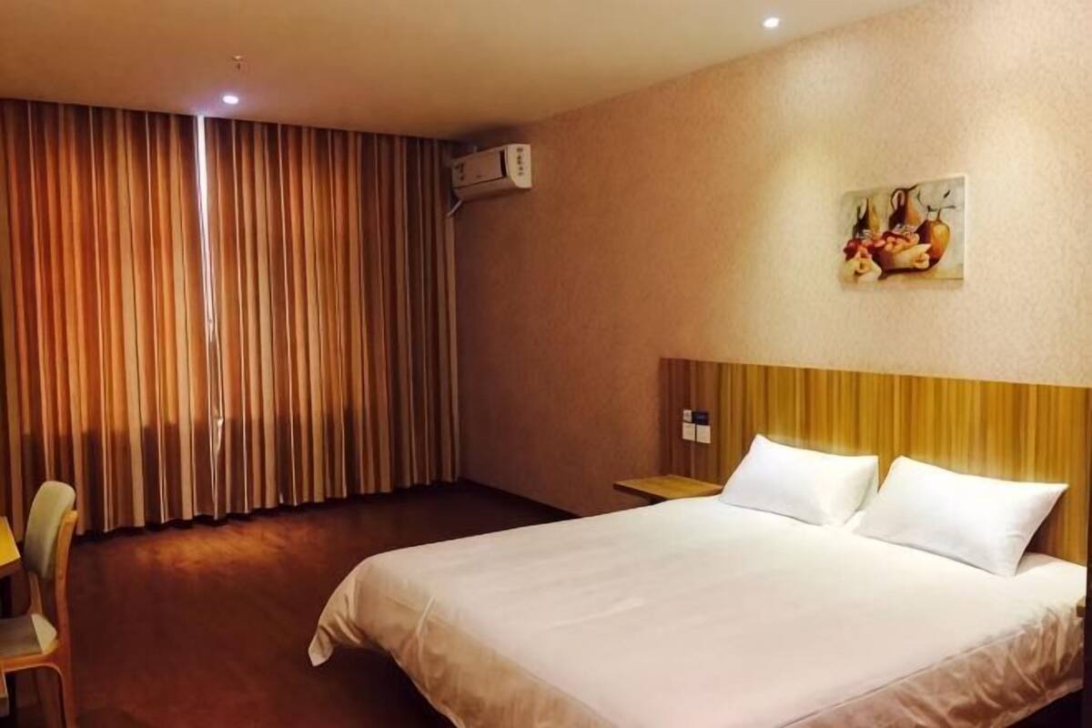 Une chambre d’hôtel avec un lit, une chaise, un tableau au mur et un appareil de climatisation.