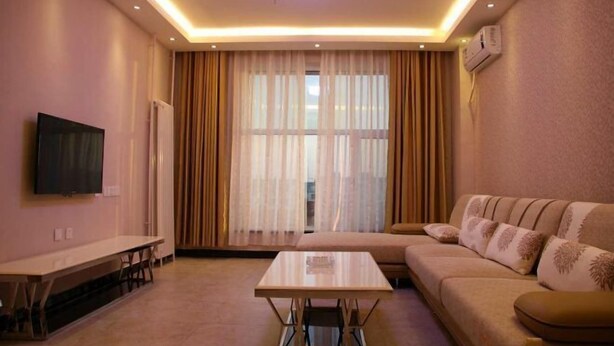 A modern living room with a sofa, a coffee table, a TV, and a large window with curtains. - Eaka 365 Hotel Daming Damingfu Road (Daming)