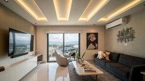 Una sala de estar moderna con un televisor grande, asientos cómodos, una mesa de centro y vistas amplias a través de grandes ventanales.