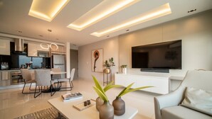 Una sala moderna con sofá, una mesa de centro y televisor. Cuenta con una zona de cocina con mesa y sillas.