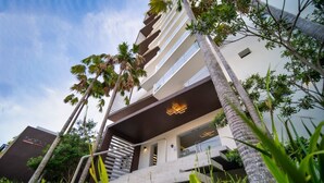 Un hotel moderno con una escalera que conduce a la entrada, rodeado de palmeras y follaje.