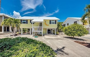 Une maison à deux étages dotée d’une fenêtre en forme de banane, entourée d’un jardin bien entretenu et de palmiers.
