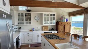 Uma cozinha moderna com armários brancos, uma ilha de madeira com pia e vista para o oceano.