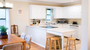 A modern kitchen with white cabinetry, a central island with stools, a microwave, and a sink. - A Tasteful Historic 4 Bedroom Home (Oklahoma City)