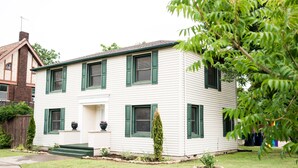 A two-story house with a front porch, green shutters, and a small garden. - A Tasteful Historic 4 Bedroom Home (Oklahoma City)