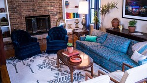 A cozy living room with a brick fireplace, a blue sofa, two blue armchairs, and a patterned rug. - A Tasteful Historic 4 Bedroom Home (Oklahoma City)