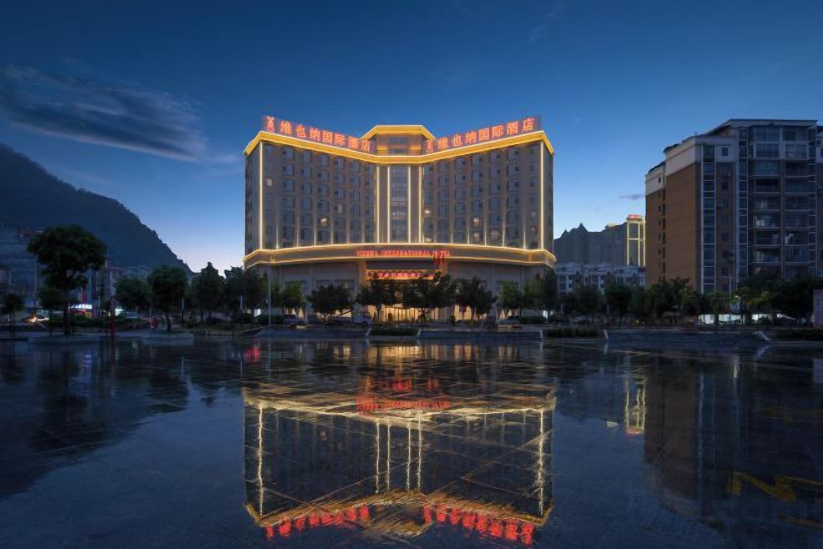 A multi-story hotel with a reflective pool in front, surrounded by other buildings.