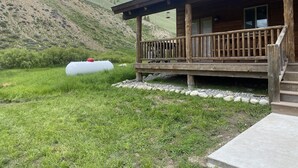 Een houten hut met een veranda, omgeven door een grasveld en een heuvel.