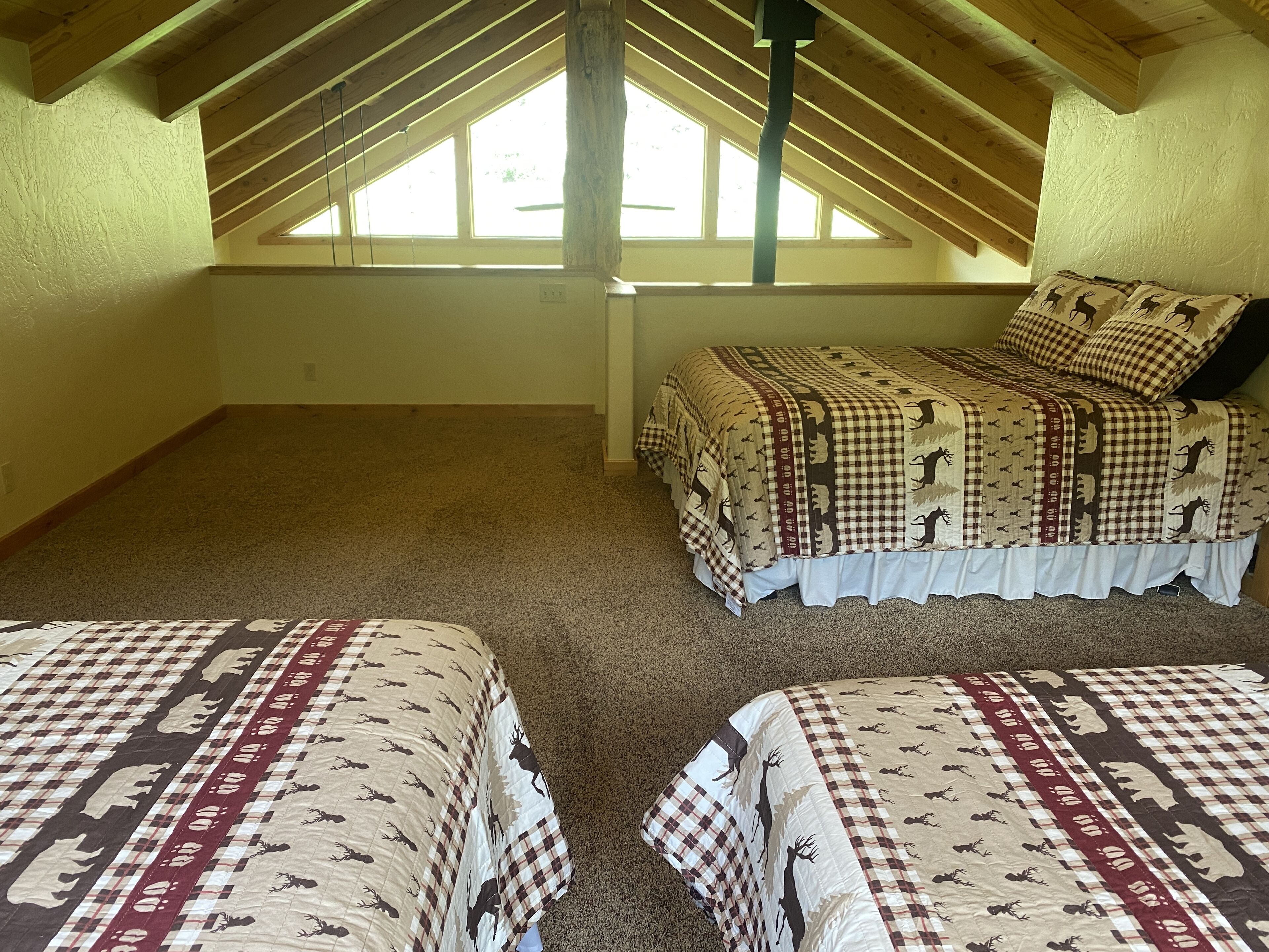 A bedroom with a sloped ceiling, a large window, and a bed with a checkered blanket.