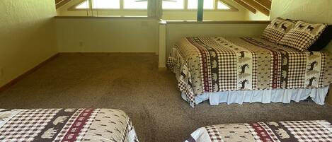 A bedroom with a sloped ceiling, a large window, and a bed with a checkered blanket.