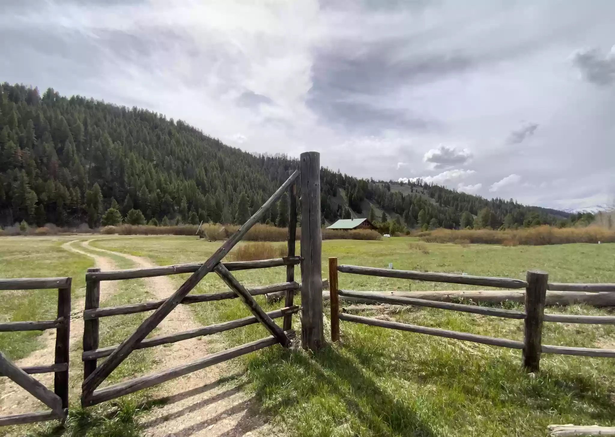 Ein hölzernes Tor in ländlicher Umgebung, ein Feldweg führt hindurch.