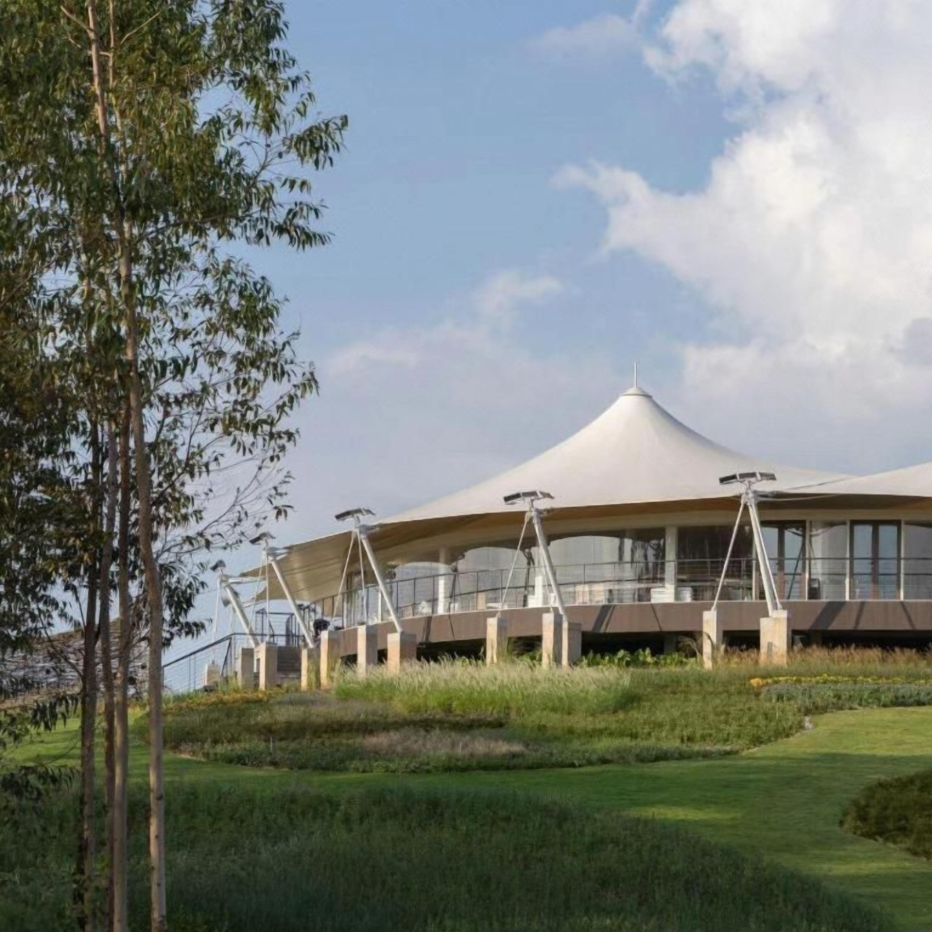 A modern building with a unique dome-like roof structure, surrounded by greenery and trees.