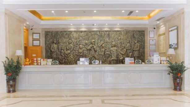A reception area with a marble reception desk, a large wall mural, and potted plants. - Vienna Hotel (Luofu Mountain Scenic Area High-Speed Rail Station Branch) (Boluo)