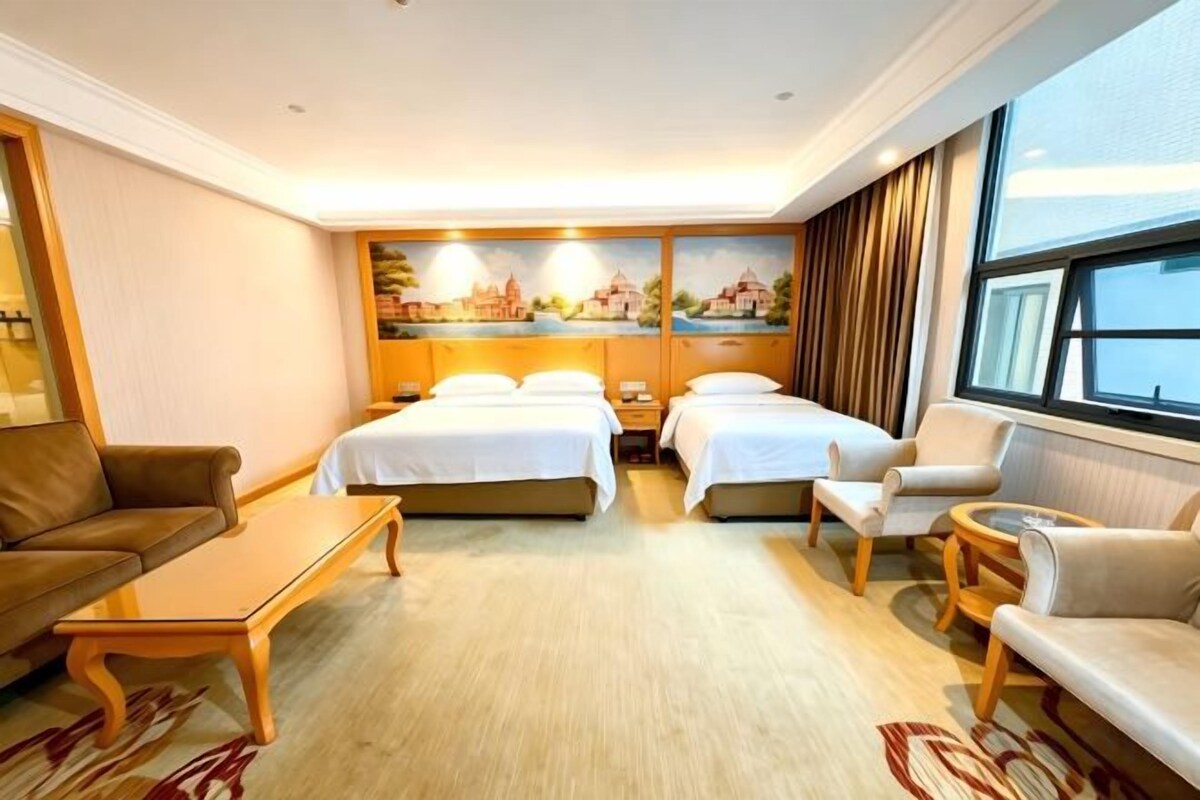 A hotel room with two beds, a sofa, a coffee table, and a painting on the wall.