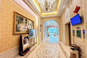 A hotel lobby with a chandelier, framed artwork, a television, and a patterned floor. - Vienna Hotel (Luofu Mountain Scenic Area High-Speed Rail Station Branch) (Boluo)