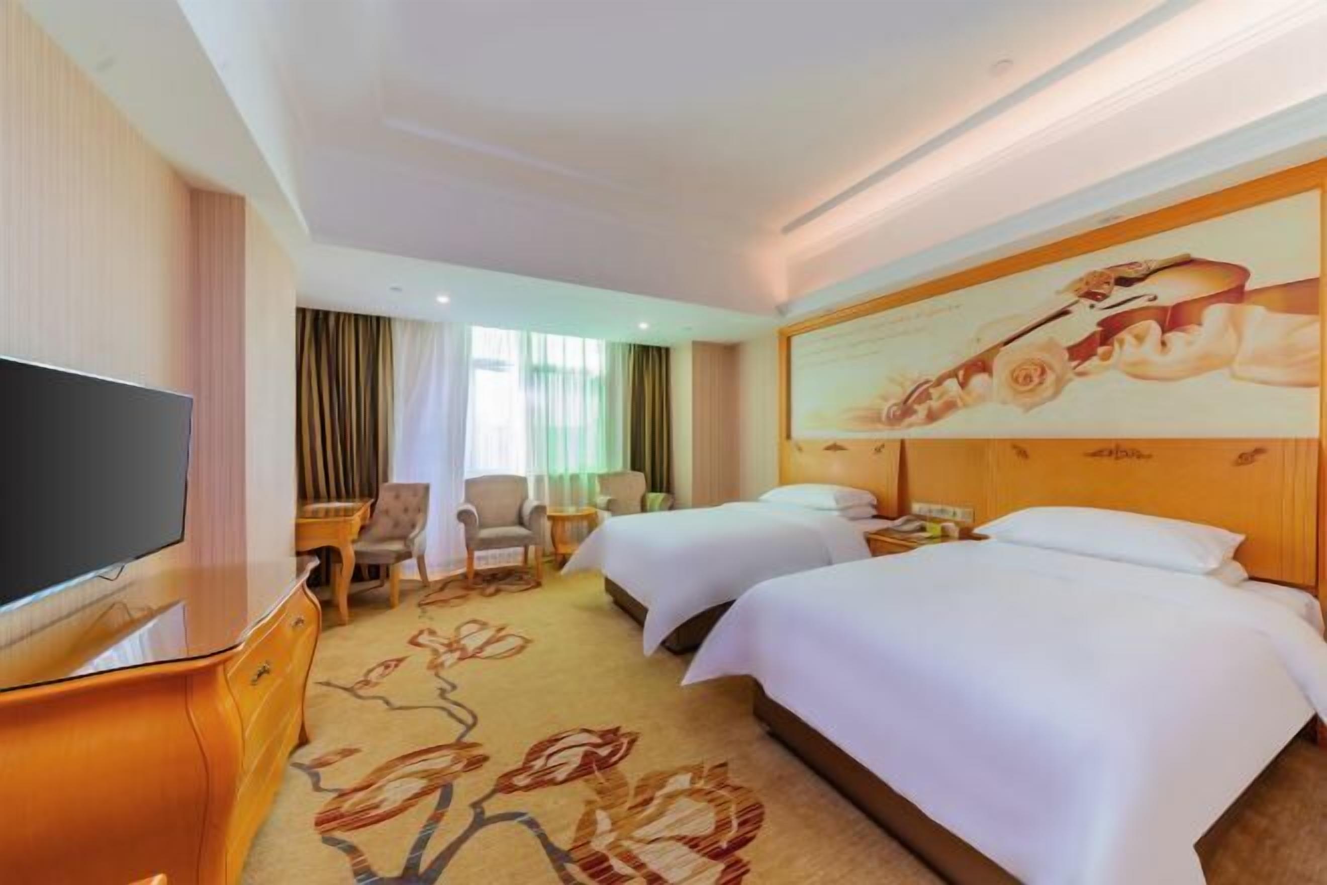 A hotel room with two beds, a TV, a desk, and a chair.