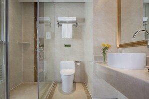 Une salle de bain moderne avec une douche à parois de verre, des toilettes blanches, un lavabo avec un miroir et un petit vase avec des fleurs.