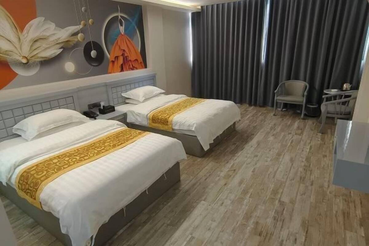 A hotel room with two beds, a mural on the wall, a grey curtain, and a small table with a chair.