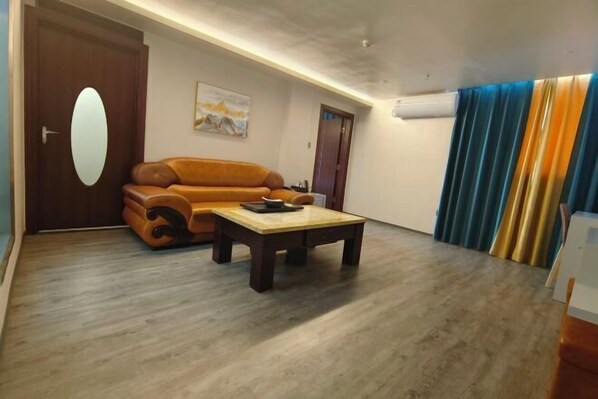 A room with a brown leather sofa, a wooden coffee table, a painting on the wall, and a door with a round mirror. - Anxi Ganglong Grand Hotel (Anxi)