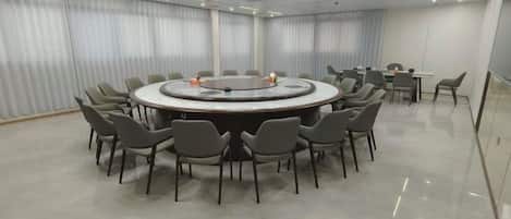 A conference room with a round table surrounded by chairs, a whiteboard, and a projector.