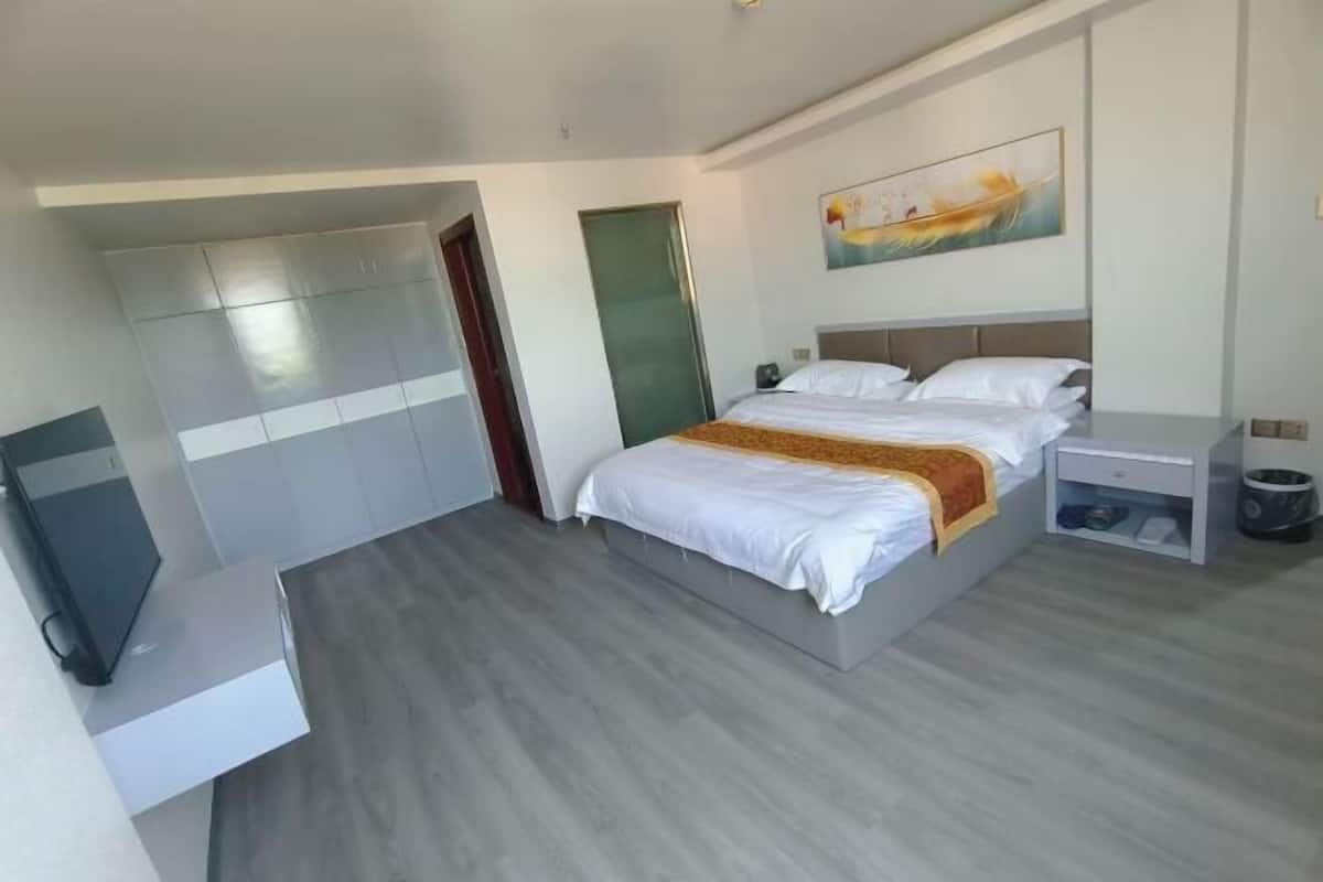 A modern hotel room with a bed, a TV, a wardrobe, and a painting on the wall.