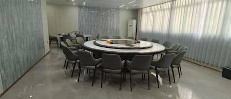A conference room with a round table surrounded by chairs, a small table with a few items, and a window with blinds.