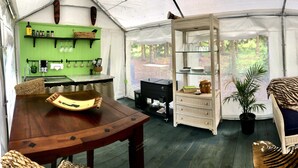 A tented room with a dining table, wicker furniture, a zebra-patterned sofa, and a green shelf with various items. - Glamping on a Safari (Wendover)