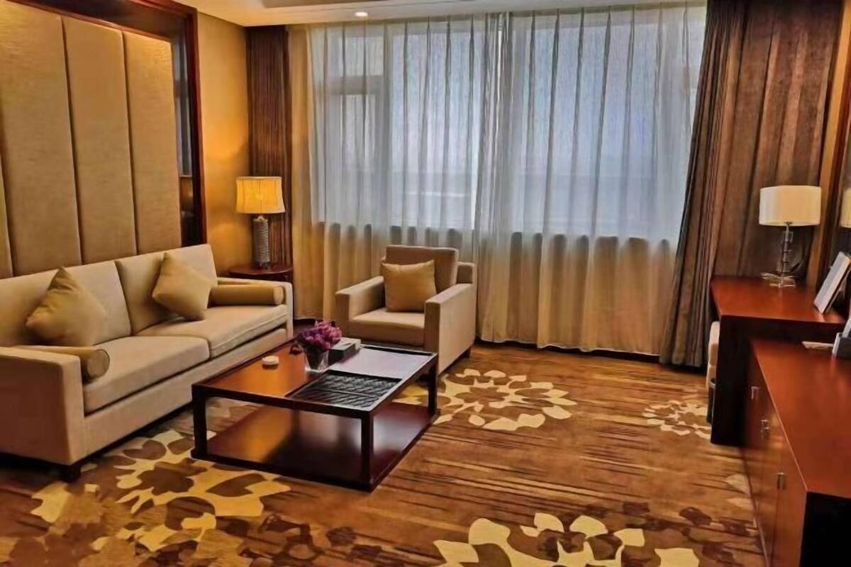 A hotel room with a sofa, armchair, and a small table with a lamp.