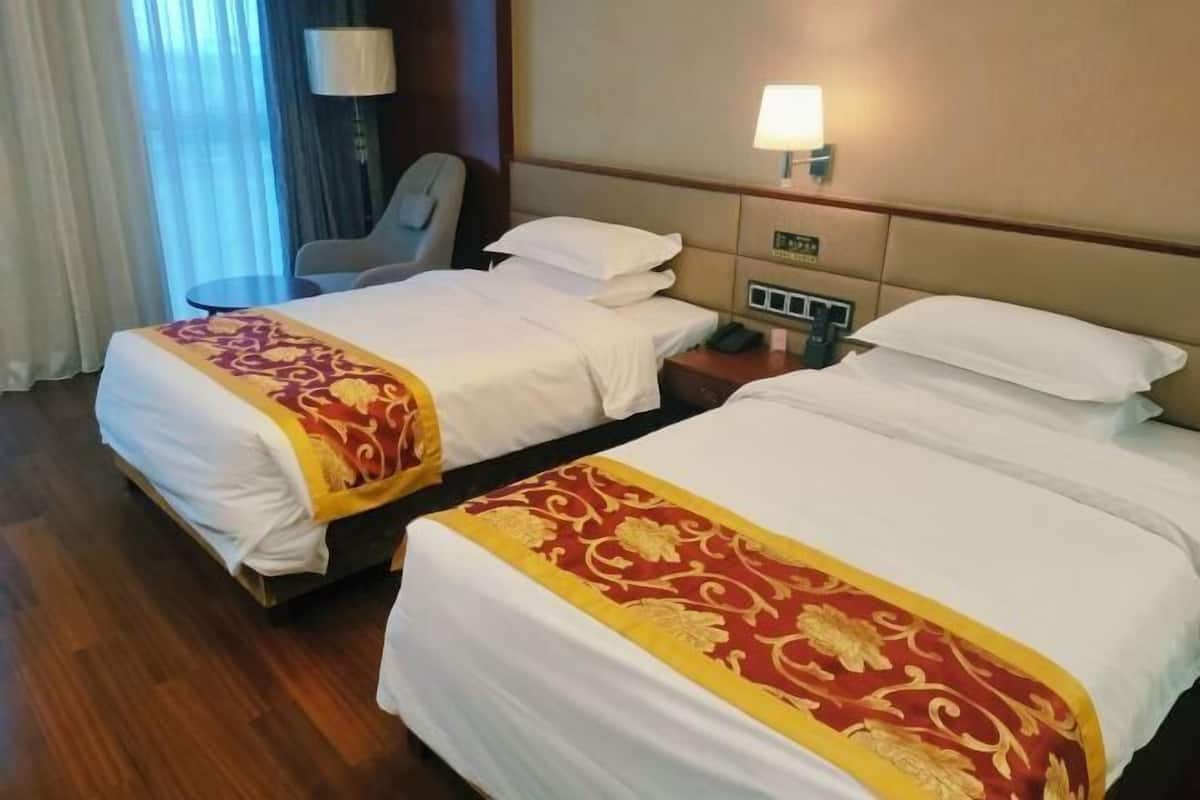 A hotel room with two beds, a desk, a chair, a lamp, and a window with curtains.