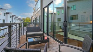 Un appartement moderne doté d’un balcon, meublé avec des meubles en osier et muni d’une porte vitrée donnant sur un espace extérieur privatif.