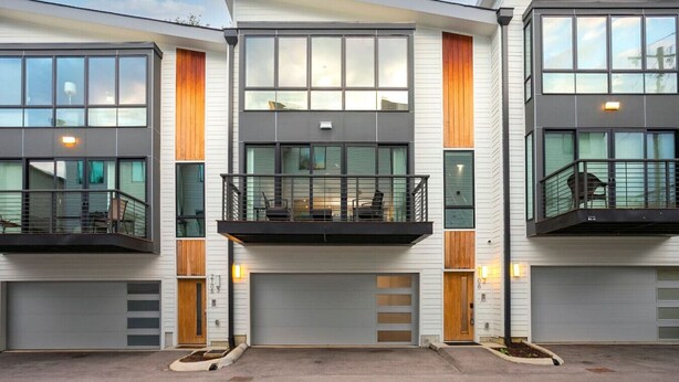 Une maison moderne à deux étages, dotée d’un balcon à l’étage supérieur, de grandes fenêtres et d’un garage.