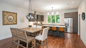 Une cuisine moderne avec un coin repas, comprenant une table et des chaises en bois, un four encastré et une grande fenêtre donnant sur un paysage verdoyant.