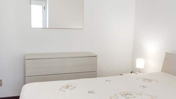 Ein Schlafzimmer mit Bett, Nachttisch, Lampe und Spiegel an der Wand.