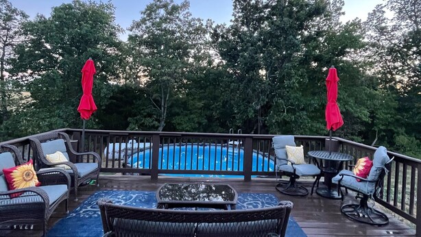 Une terrasse dotée de mobilier d’extérieur, d’une piscine et bordée d’arbres.