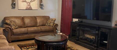 Un salon avec un canapé en cuir marron, une table basse en verre, une cheminée, un téléviseur et un ventilateur de plafond.