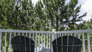 Eine Terrasse mit zwei Adirondack-Stühlen und einem kleinen Tisch, mit Blick auf ein bewaldetes Gebiet.