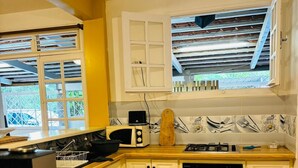 A kitchen with white cabinets, a microwave, a stove, and a window overlooking a balcony. - Spacious house with jacuzzi 5 minutes from town center. (Fort-de-France)