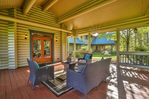 Une cabane en rondins dotée d’un porche aménagé avec des meubles en osier et une porte en verre.