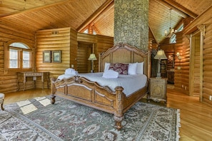 Une chambre aménagée dans un chalet en rondins, avec un grand lit, des murs en bois, un pilier en pierre et un lustre de style rustique.