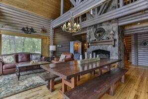 L’intérieur d’une cabane en rondins, avec une table à manger en bois, un canapé en cuir et une cheminée en pierre.