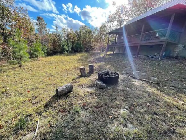 A grassy outdoor area with a fire pit, wooden stumps, and a building with a metal roof.