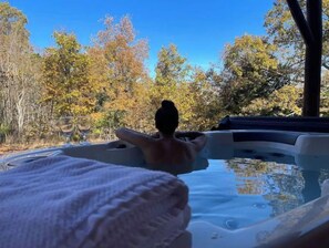 A hot tub with a person relaxing, surrounded by autumn foliage.